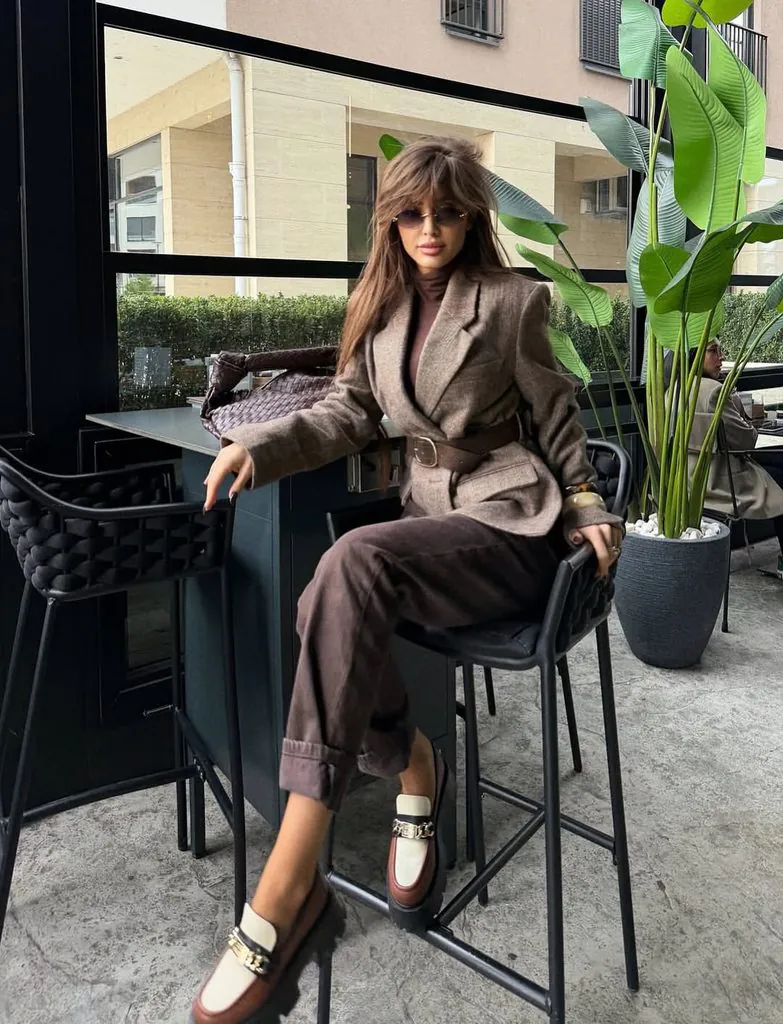 woman sitting on a bar stool wearing a belted brown blazer and matching trousers