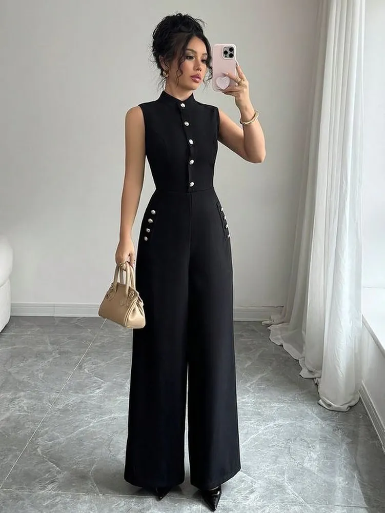 woman standing in a black sleeveless jumpsuit with gold buttons holding a small purse