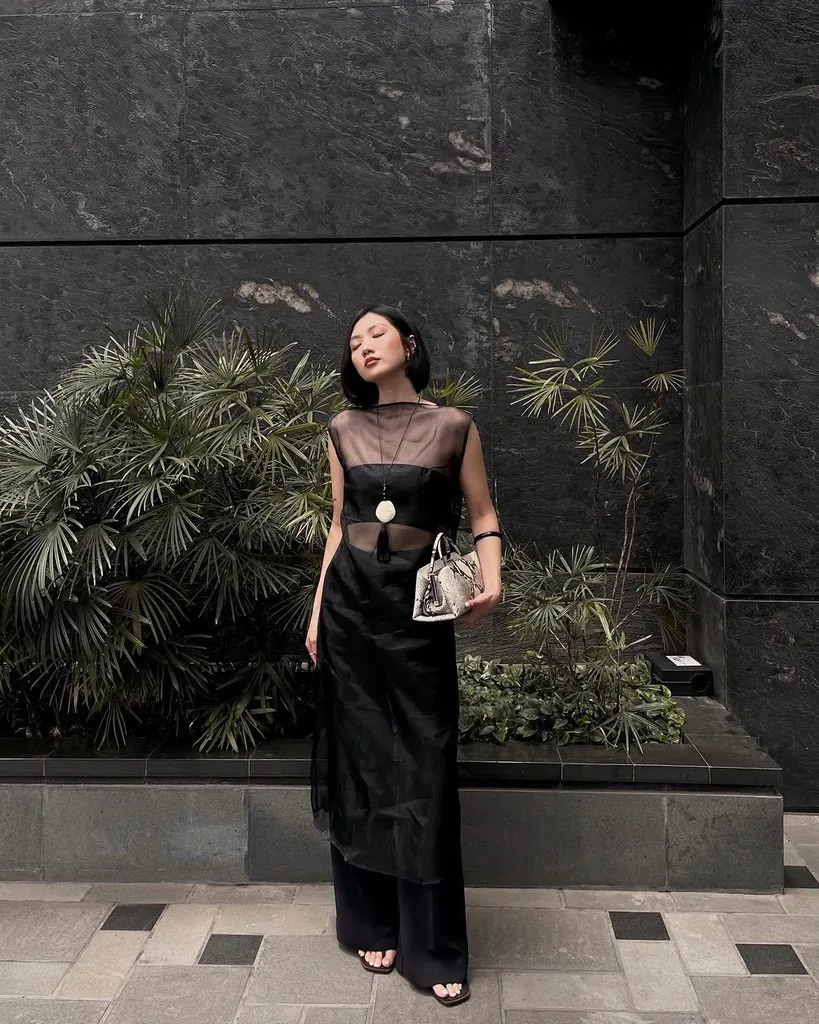 woman wearing a sheer black overlay midi dress with wide-leg pants and a clutch bag