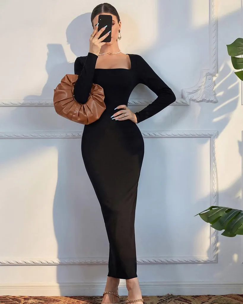 woman posing in a black long-sleeve maxi dress holding a brown pleated handbag