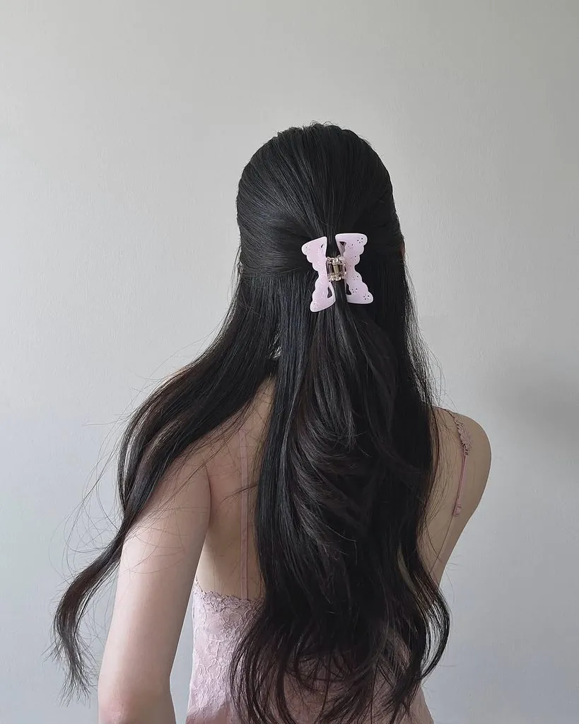 long dark wavy hair in a half-up style secured with a pink butterfly claw clip