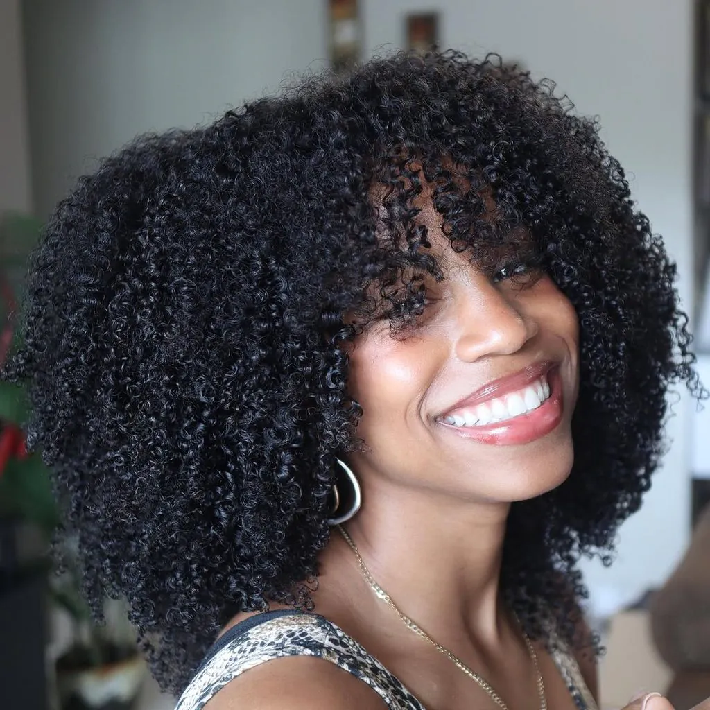 smiling black woman showing off her voluminous curly hair with curly bangs