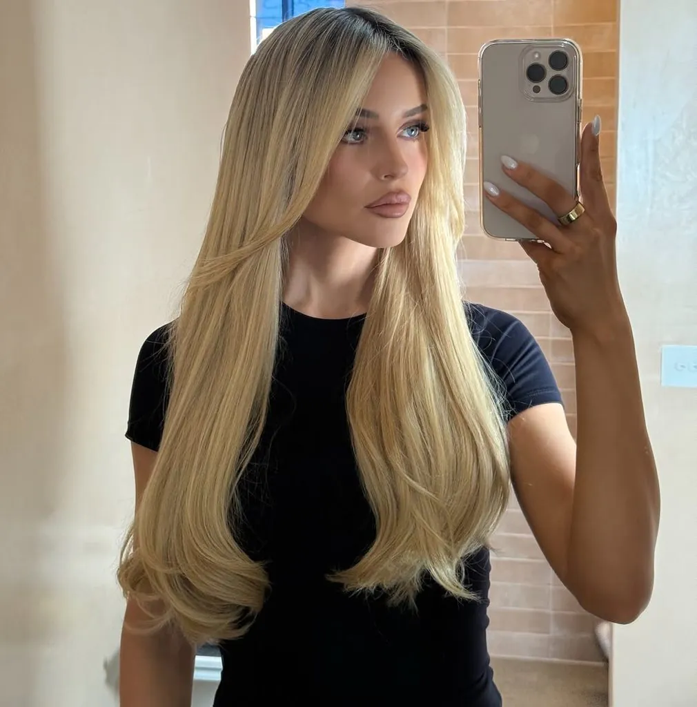 blonde woman with very long layered hair parted in the middle taking a selfie
