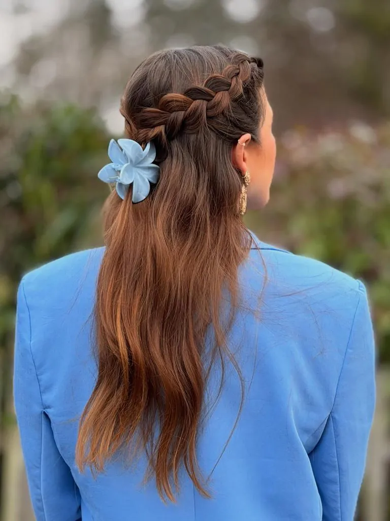 half-up braided summer hairstyle on brown hair secured with a blue flower claw clip
