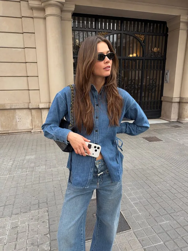 woman wearing denim on denim outfit with sunglasses holding white phone on street