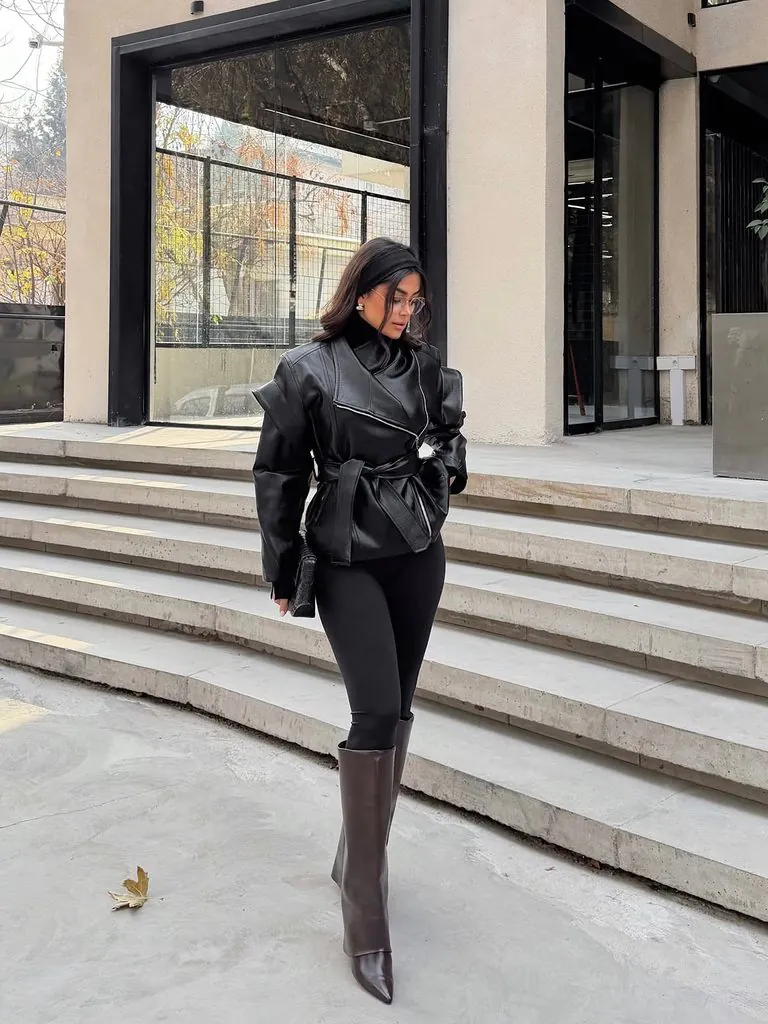 woman wearing black leather wrap jacket and tall boots on outdoor stairs