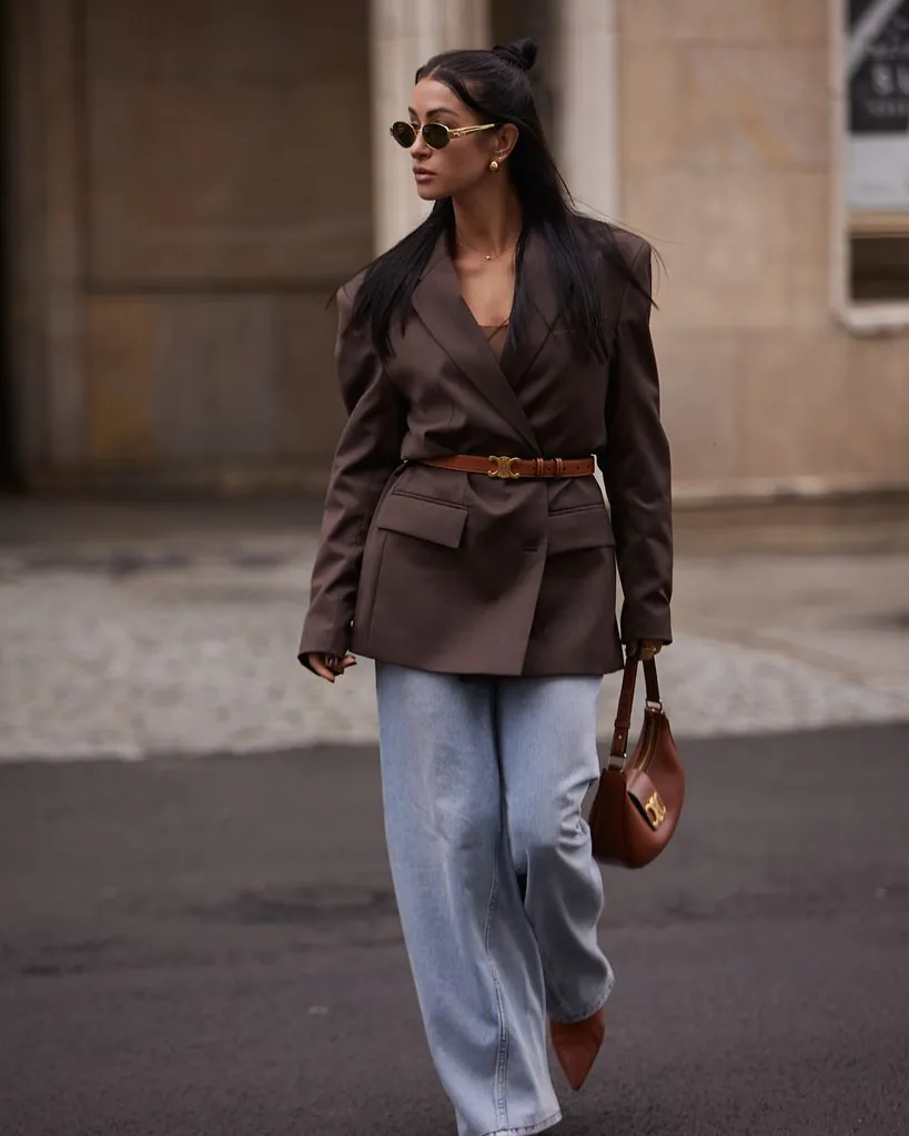 woman wearing belted brown blazer and light jeans on city sidewalk