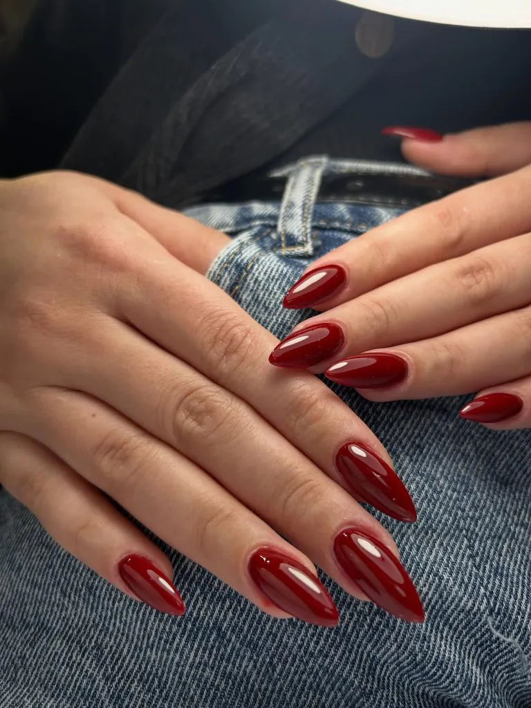 glossy classic deep red almond nails resting over denim jeans