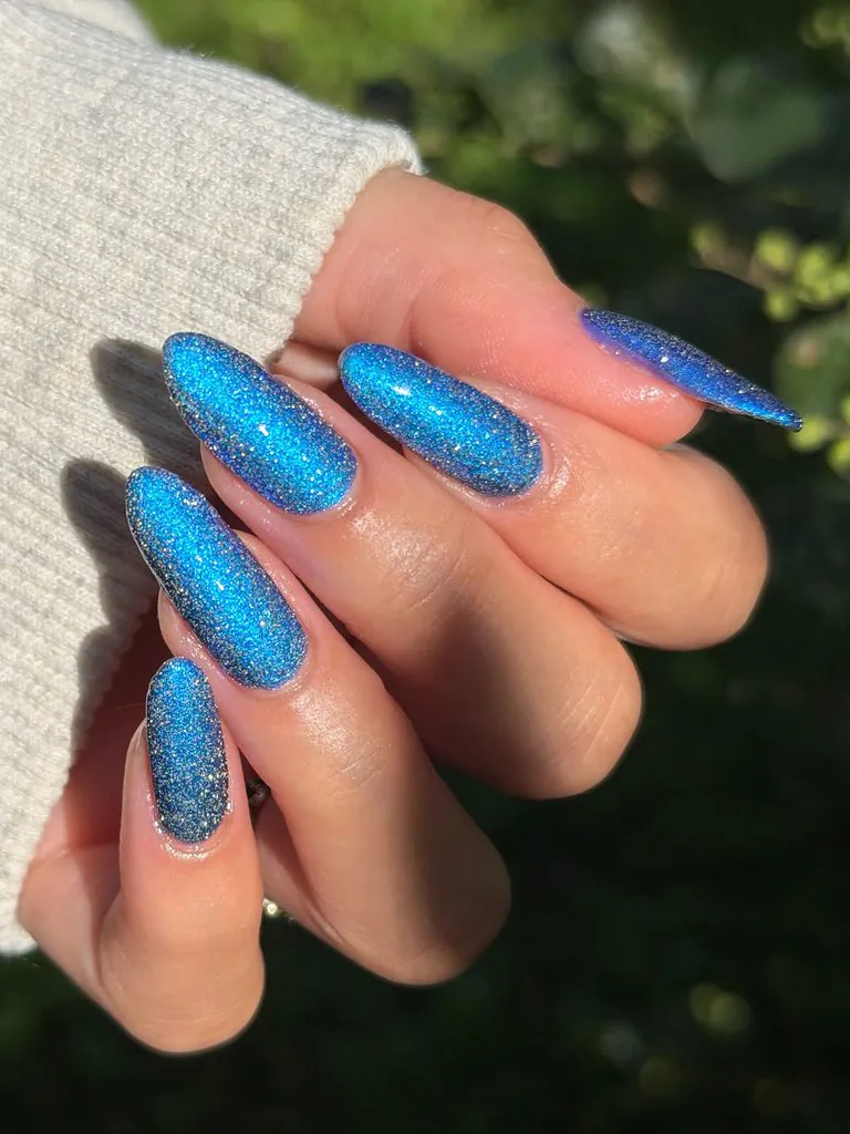 sparkling blue glitter almond nails on a hand wearing a white sweater