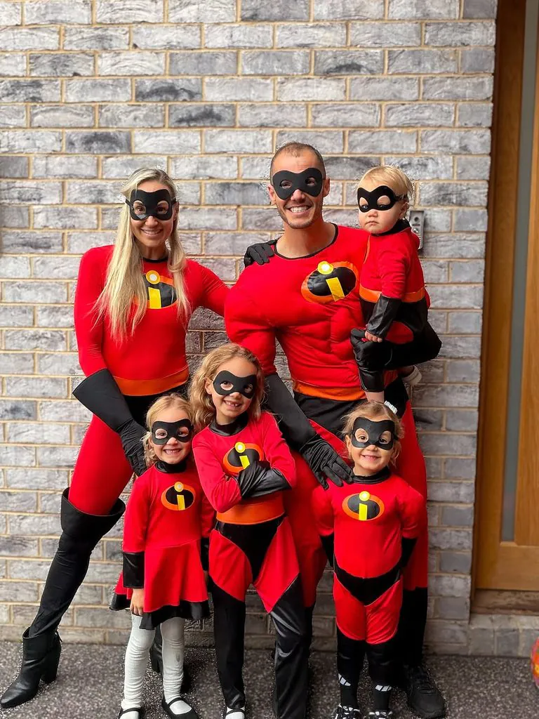 family dressed as the incredibles superheroes posing together in front of a brick wall