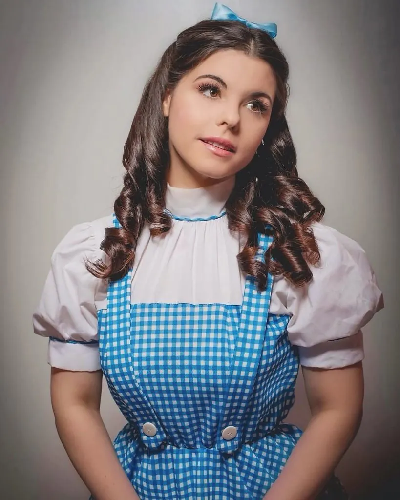 woman dressed in a blue gingham dorothy costume with curled dark hair and bow headband