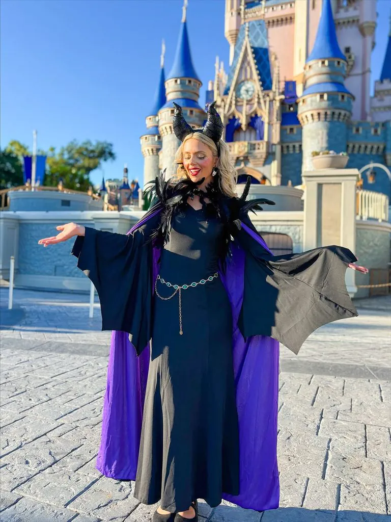 woman posing in a black and purple maleficent costume in front of a fairytale castle