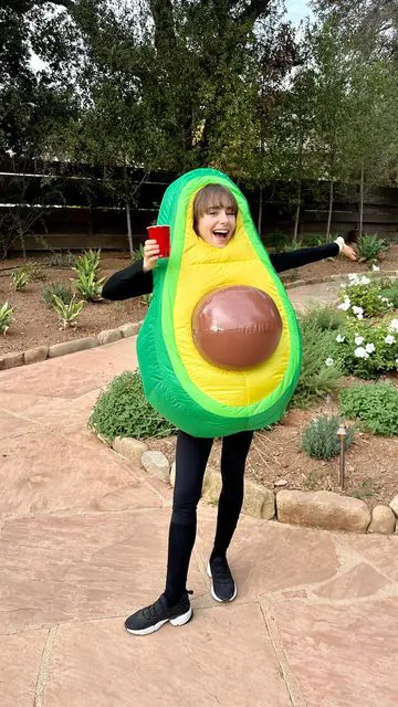 woman wearing a green inflatable avocado costume while holding a red cup outdoors