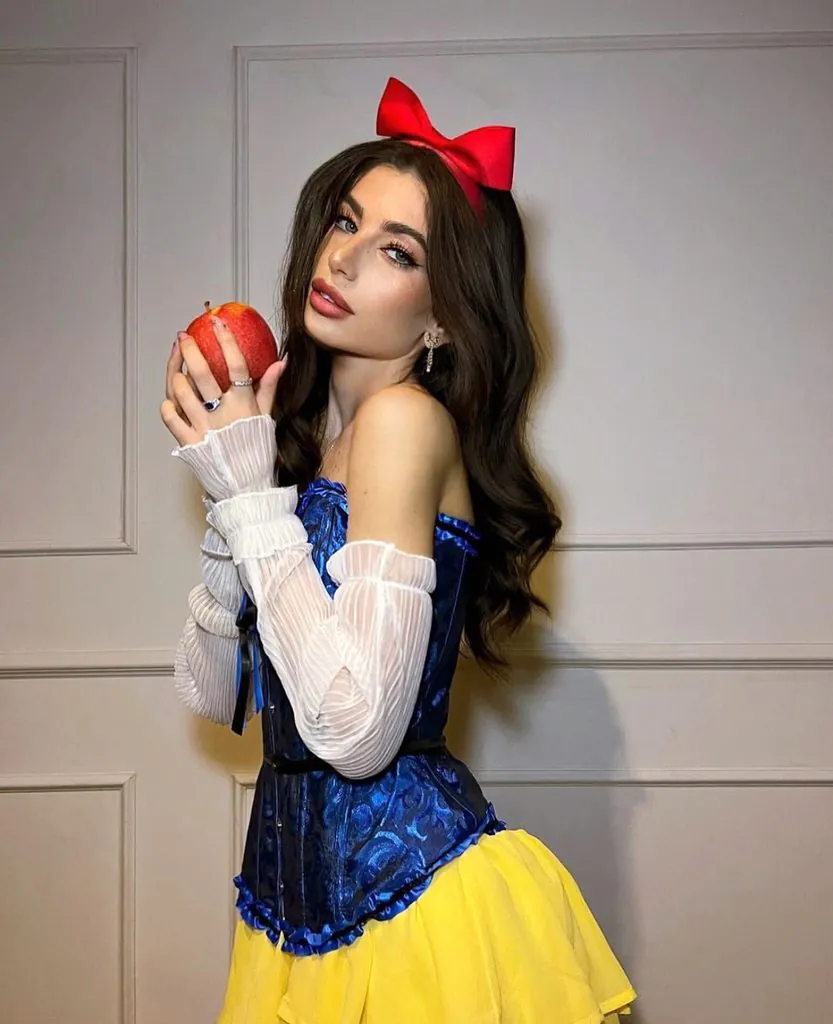 woman dressed as snow white holding a red apple while wearing a corset dress