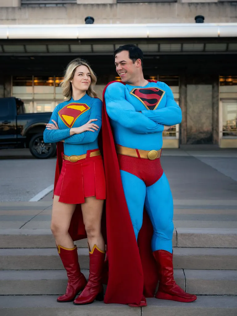 man and woman dressed in superman and supergirl halloween costumes posing on steps