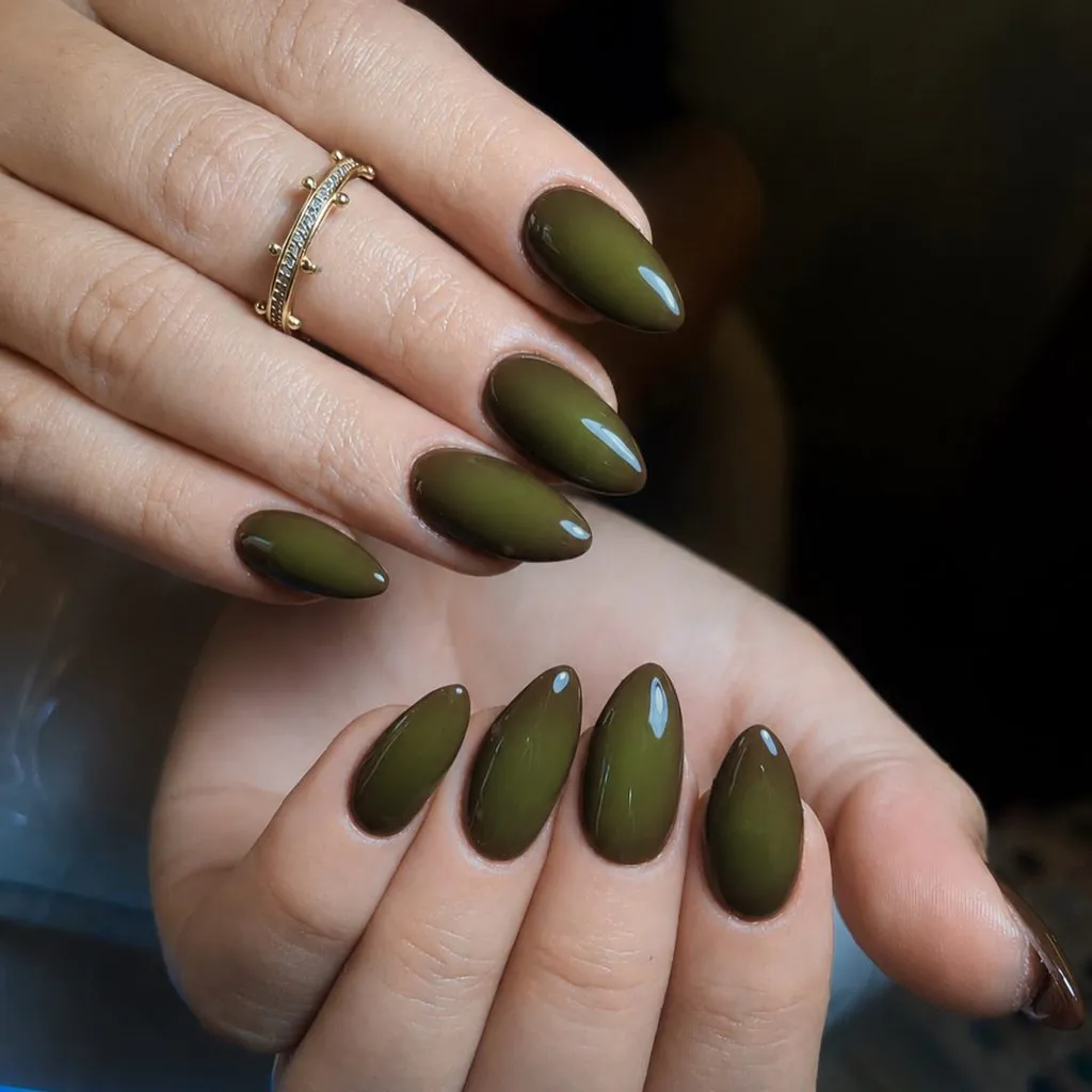 dark olive green glossy almond nails on hands with a gold ring