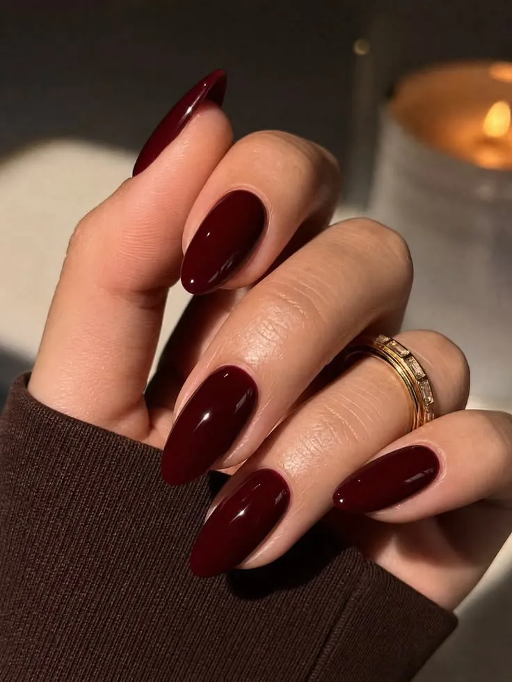 deep glossy burgundy red oval nails resting on a brown knit sleeve