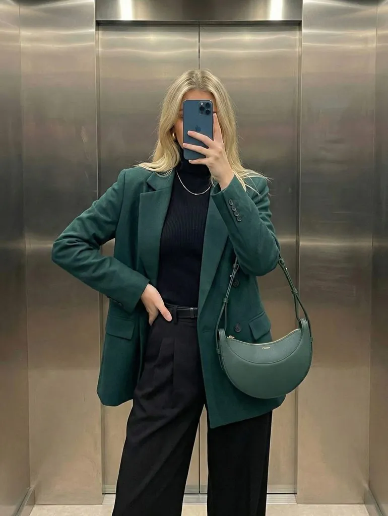 woman in dark green blazer black turtleneck and matching green curved shoulder bag
