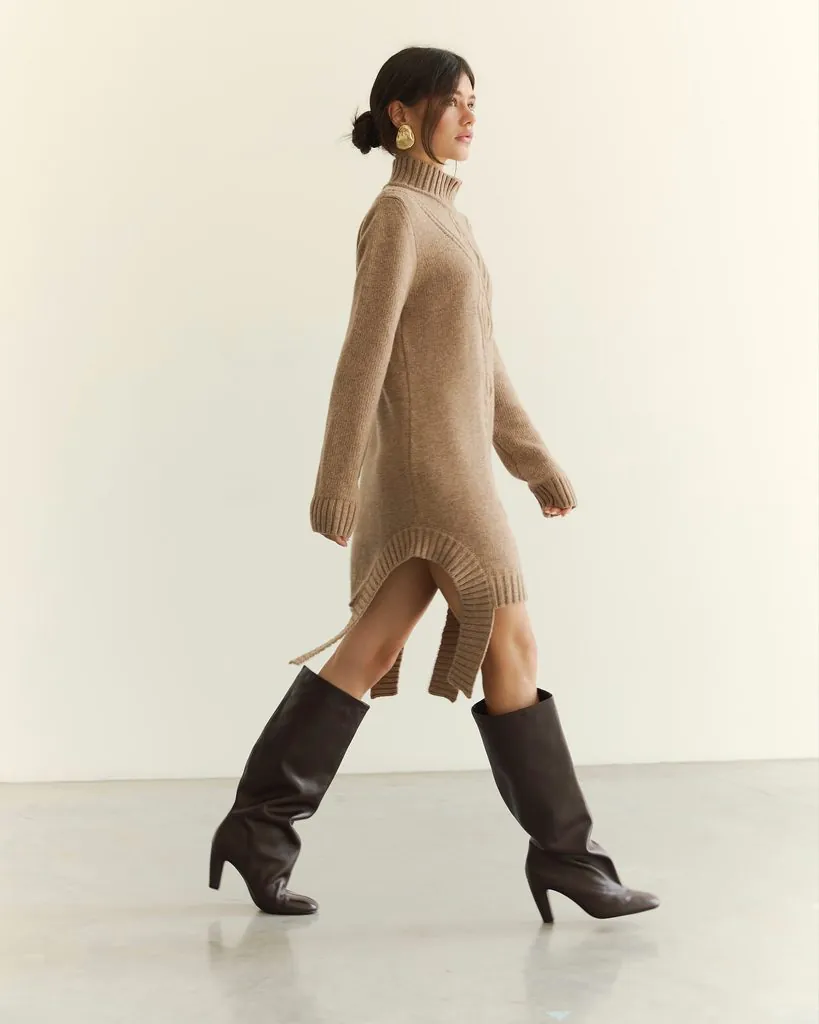 woman walking in beige turtleneck sweater dress with knee high dark brown boots
