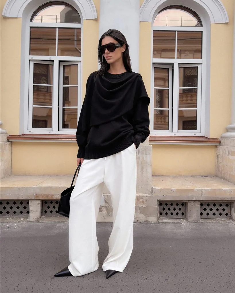 woman standing outdoors wearing draped black sweater white wide leg pants and sunglasses